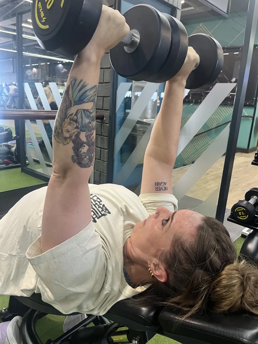 Megan pressing dumbbells, her &ldquo;never again&rdquo; tattoo visible